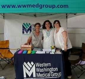 3 women posing as a group behind a WWMG booth | WWMG