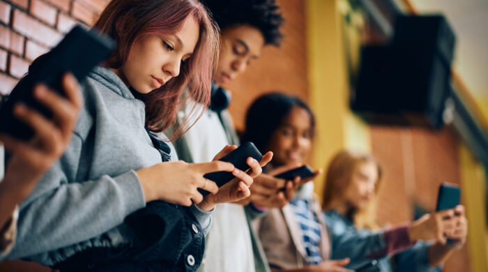 High school student and her friends using their smart phones in a hallway.