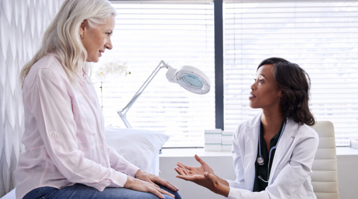 Mature Woman In Consultation With Female Doctor Sitting On Examination Couch In Office