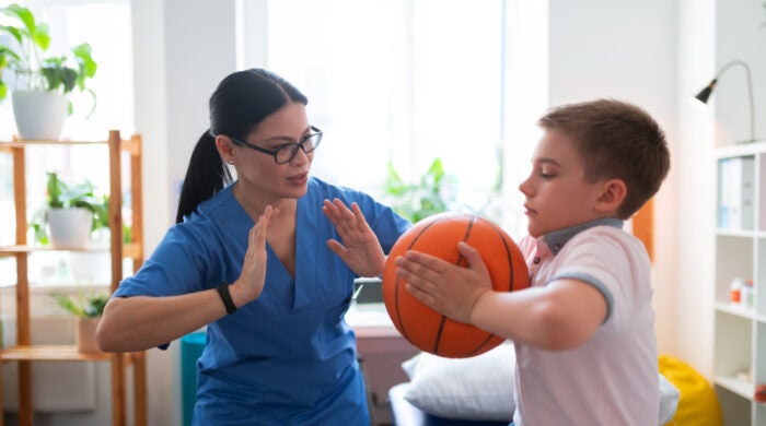 Pushing hands. Active dark-haired nurse in blue uniform showing example of exercise with ball