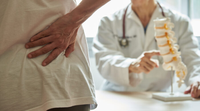 A male doctor explaining lumbar anatomy to female patient complaining of back pain at medical clinic