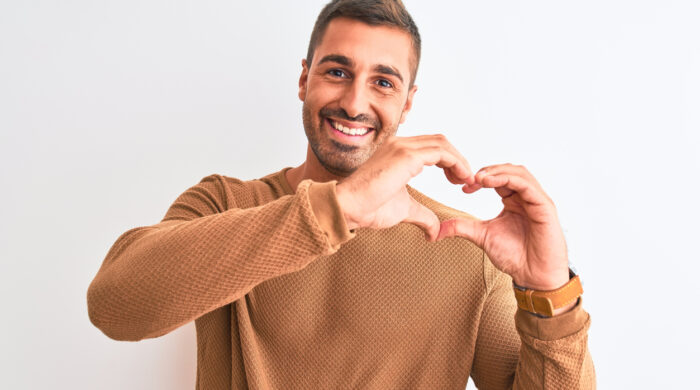 Young handsome elegant man wearing winter sweater over isolated background smiling in love showing heart symbol and shape with hands. Romantic concept.