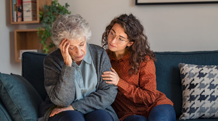 Caring daughter comforting frustrated unhappy senior woman. Loving adult granddaughter talking to sad depressed old grandmother holding hand and comforting her. Upset widowed woman with headache consoled by her daughter.