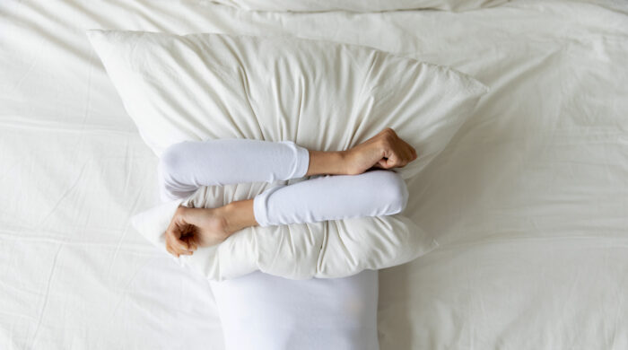 Top view depressed woman covering face with pillow, lying on bed at home alone, frustrated unhappy young female suffering from insomnia, mental or relationship problems, break up or divorce