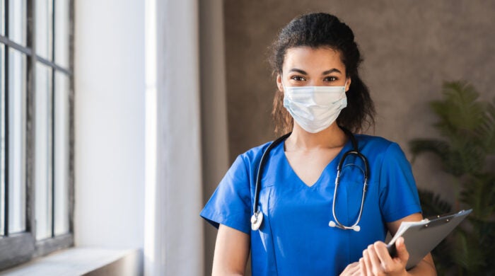 Confident young female african scrub nurse wear blue uniform, face mask,standing arms crossed in hospital hallway. Black millennial woman doctor, surgeon, medic staff professional portrait.