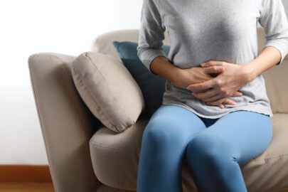 woman sitting on couch holding her stomach because it hurts