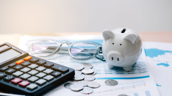 Calculator with text Tax Saving. Calculator, Piggy Bank, coins, business graph and pen on wooden table.