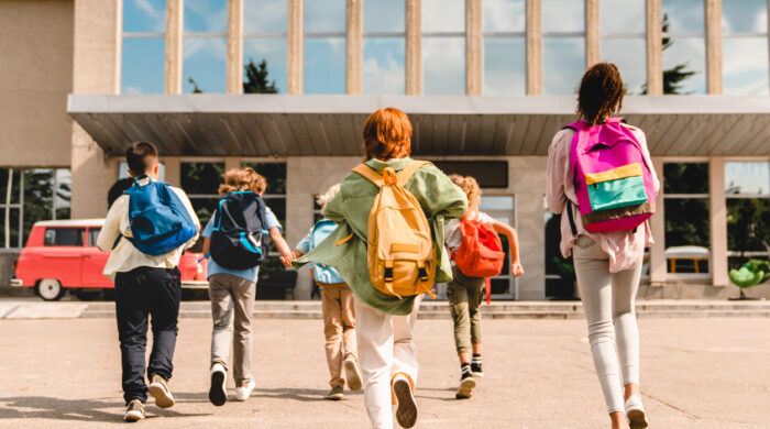 Little kids schoolchildren pupils students running hurrying to the school building for classes lessons from to the school bus. Welcome back to school. The new academic semester year start