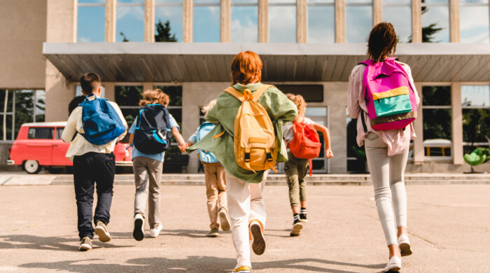 Little kids schoolchildren pupils students running hurrying to the school building for classes lessons from to the school bus. Welcome back to school. The new academic semester year start