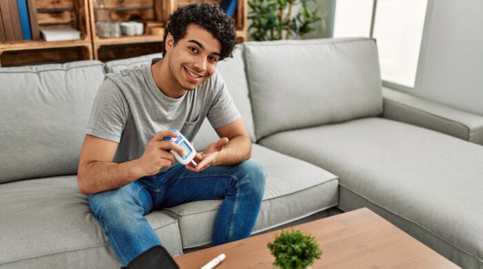 Young hispanic diabetic man measuring glucose sitting on the sofa at home.
