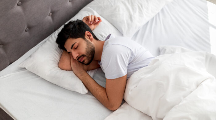 Asleep young arab man sleeping, resting peacefully in comfortable bed, lying with closed eyes, free space. Recreation, deep male sleep, time to rest and nap concept