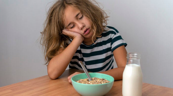 GIRL FALLS ASLEEP WHILE HAVING BREAKFAST IN THE KITCHEN. SLEEP DISORDERS IN CHILDHOOD. CHILDISH DROWSINESS CONCEPT.