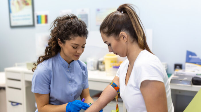 Preparation for blood test with pretty young woman by female doctor medical uniform on the table in white bright room. Nurse pierces the patient's arm vein with needle blank tube.