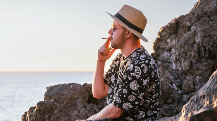 young man in profile with a casual hat smoking a joint in front of the sea