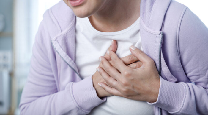 Young woman pressing on chest with painful expression. Severe heartache, having heart attack or painful cramps, heart disease