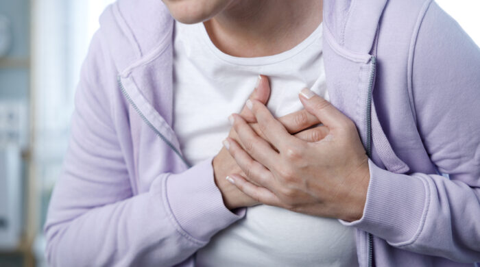 Young woman pressing on chest with painful expression. Severe heartache, having heart attack or painful cramps, heart disease