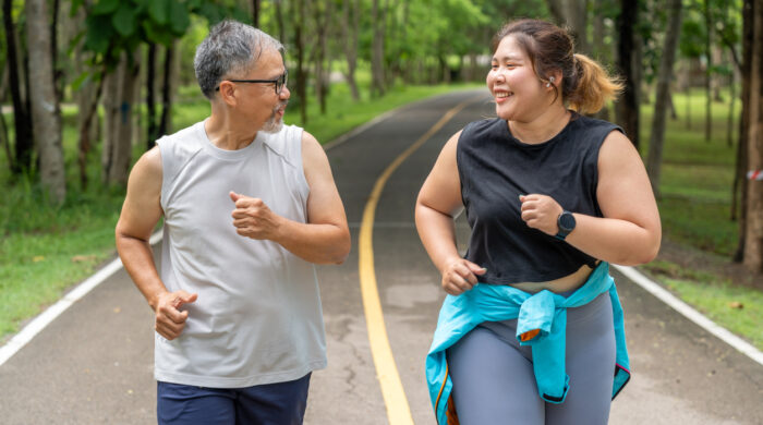 Happy middle age man and young overweight woman enjoy talking to each other during their morning run at a running track of a local park