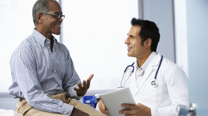 Doctor In Surgery With Male Patient Using Digital Tablet Smiling To Each Other.