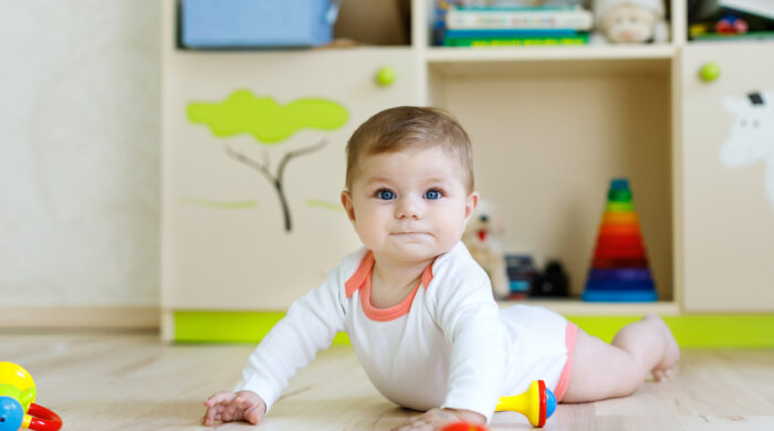 Cute happy smiling baby playing with colorful rattle toys. New born child, little girl learning crawling. Family, new life, childhood, beginning concept. Baby learning grab wooden blocks