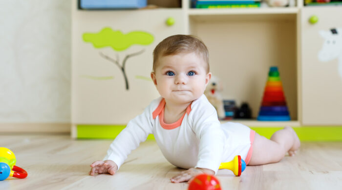 Cute happy smiling baby playing with colorful rattle toys. New born child, little girl learning crawling. Family, new life, childhood, beginning concept. Baby learning grab wooden blocks
