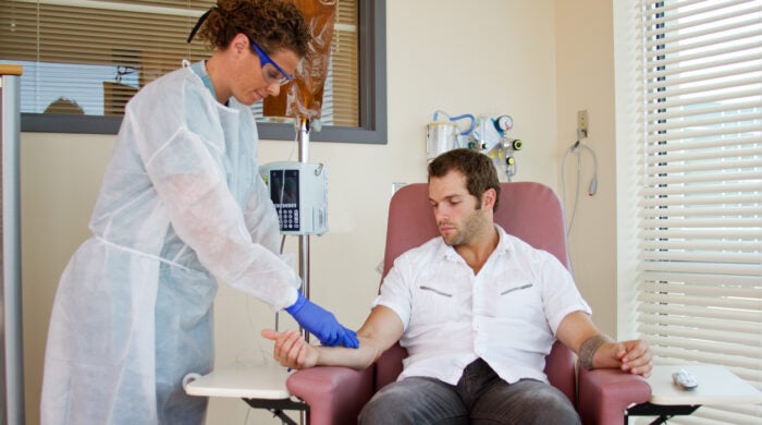 Nurse attaching IV to man's arm for patient infusion therapy in an outpatient clinic