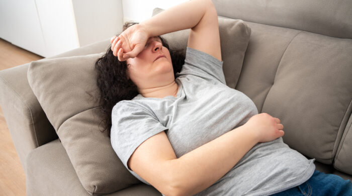 Woman lying on back on comfortable couch at home, covering eyes with hand, sleeping at daytime, feeling tired, enjoying relaxation, leisure, break, weekend. Top view
